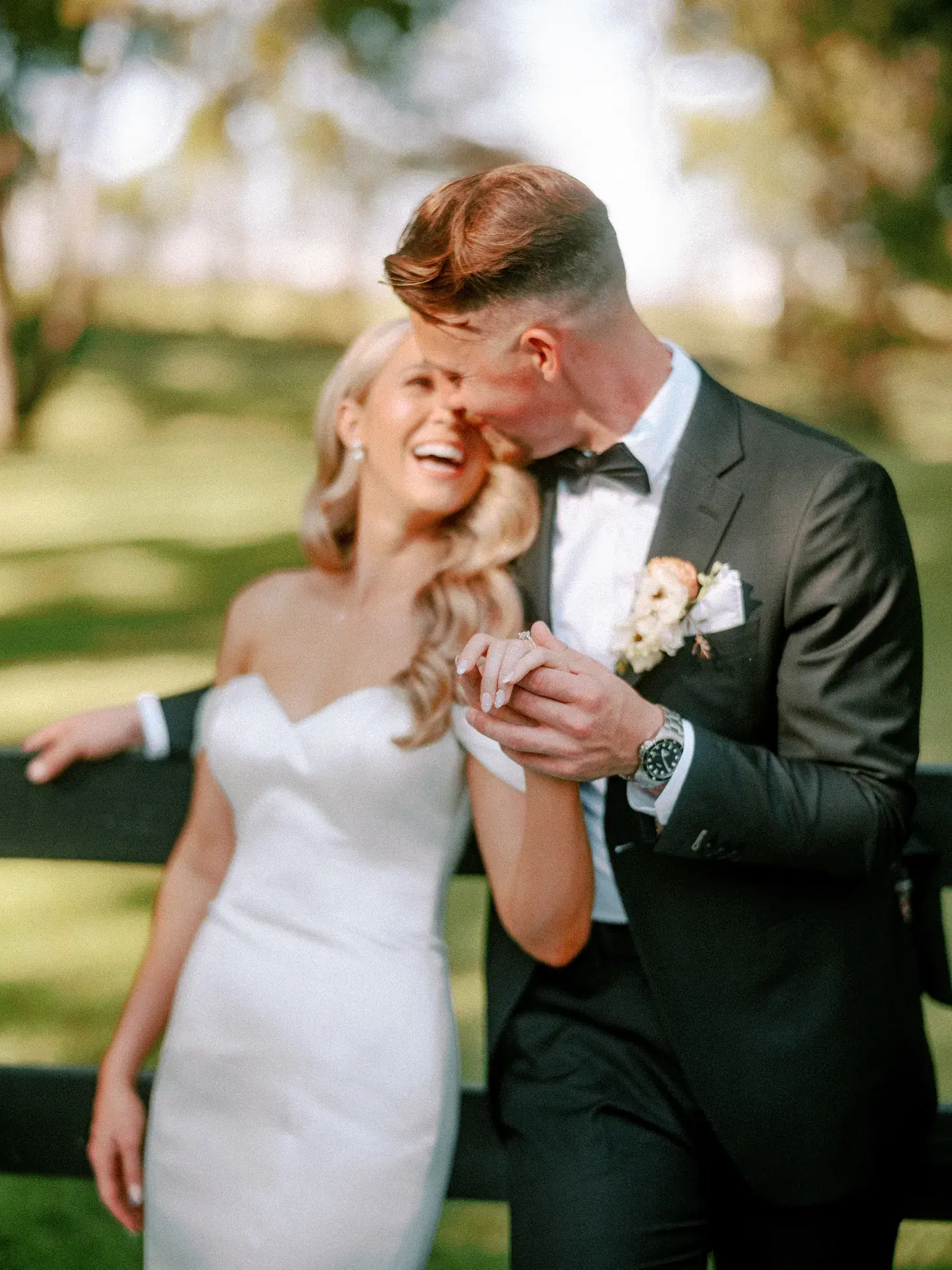 Groom kissing a laughing bride outdoors in golden light