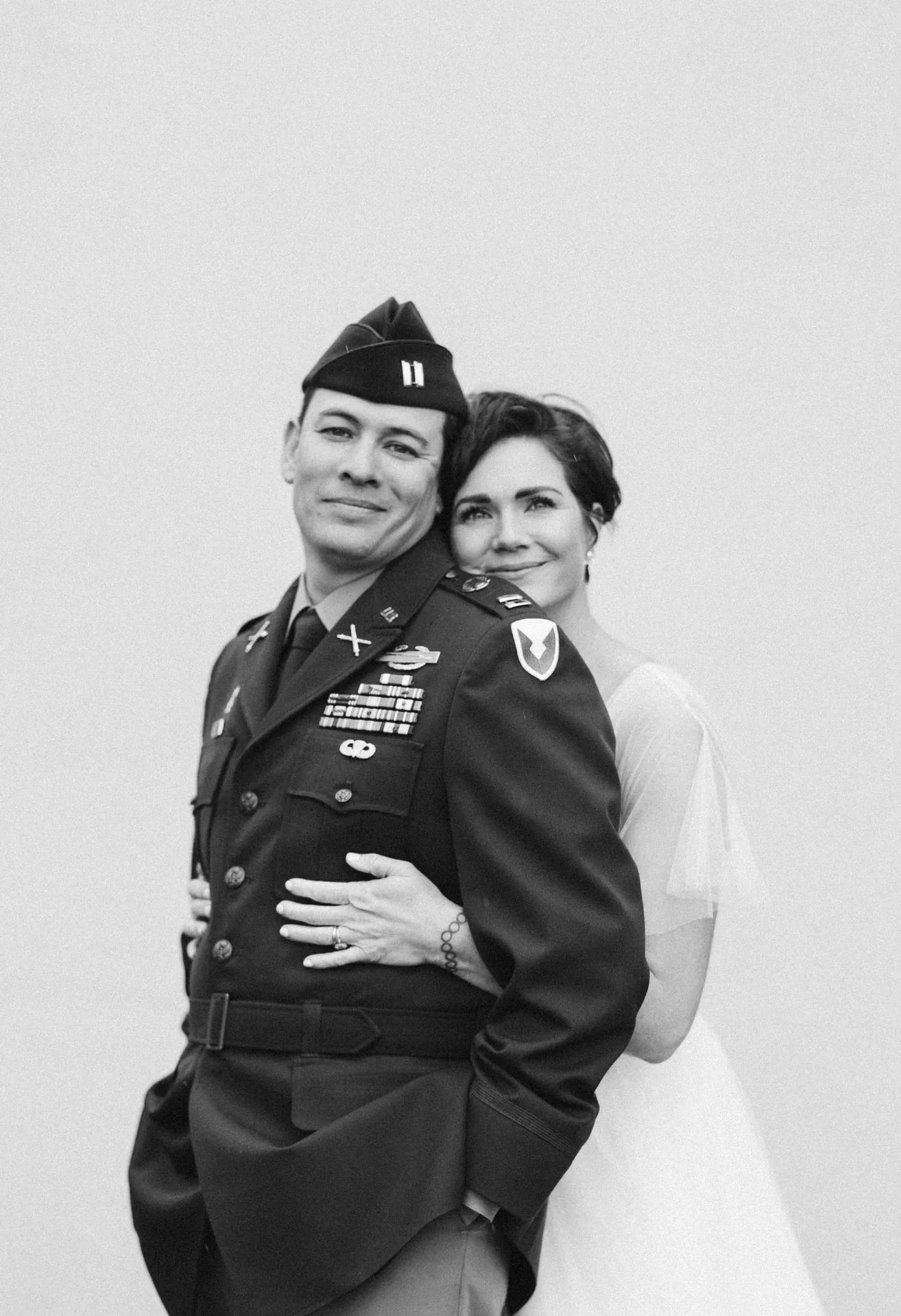 Bride embracing a groom in military dress uniform, black and white