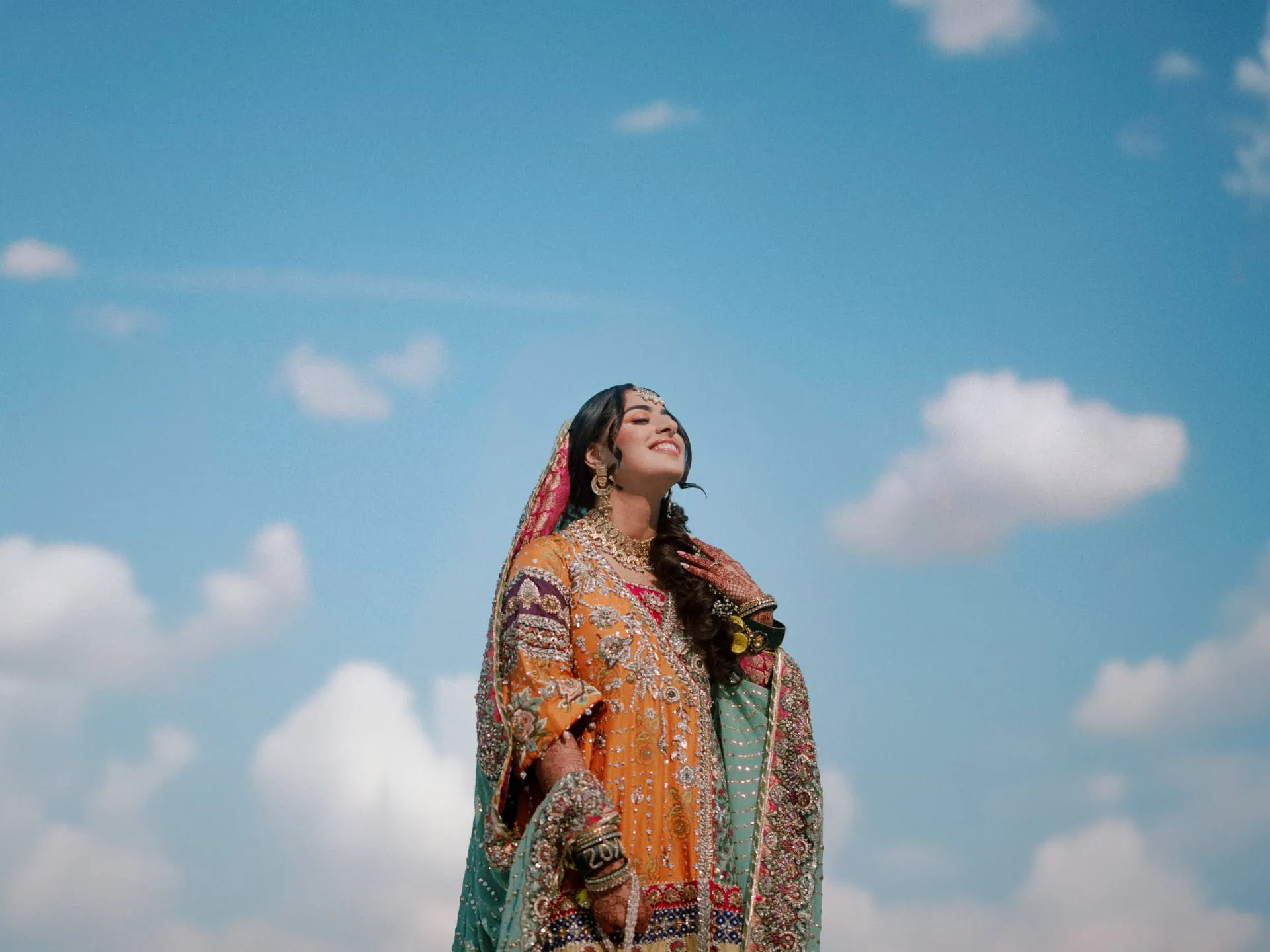 Bride in orange and gold traditional dress against a blue sky
